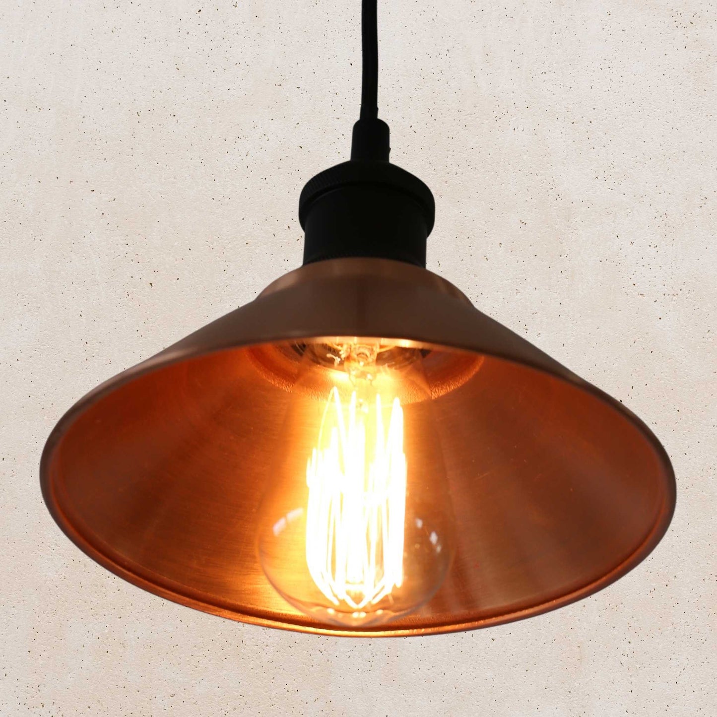 Copper pendant light with a glowing bulb against a beige background