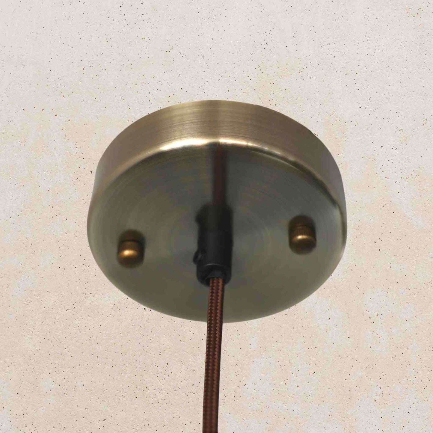 Metallic ceiling rose with wiring on a textured beige wall
