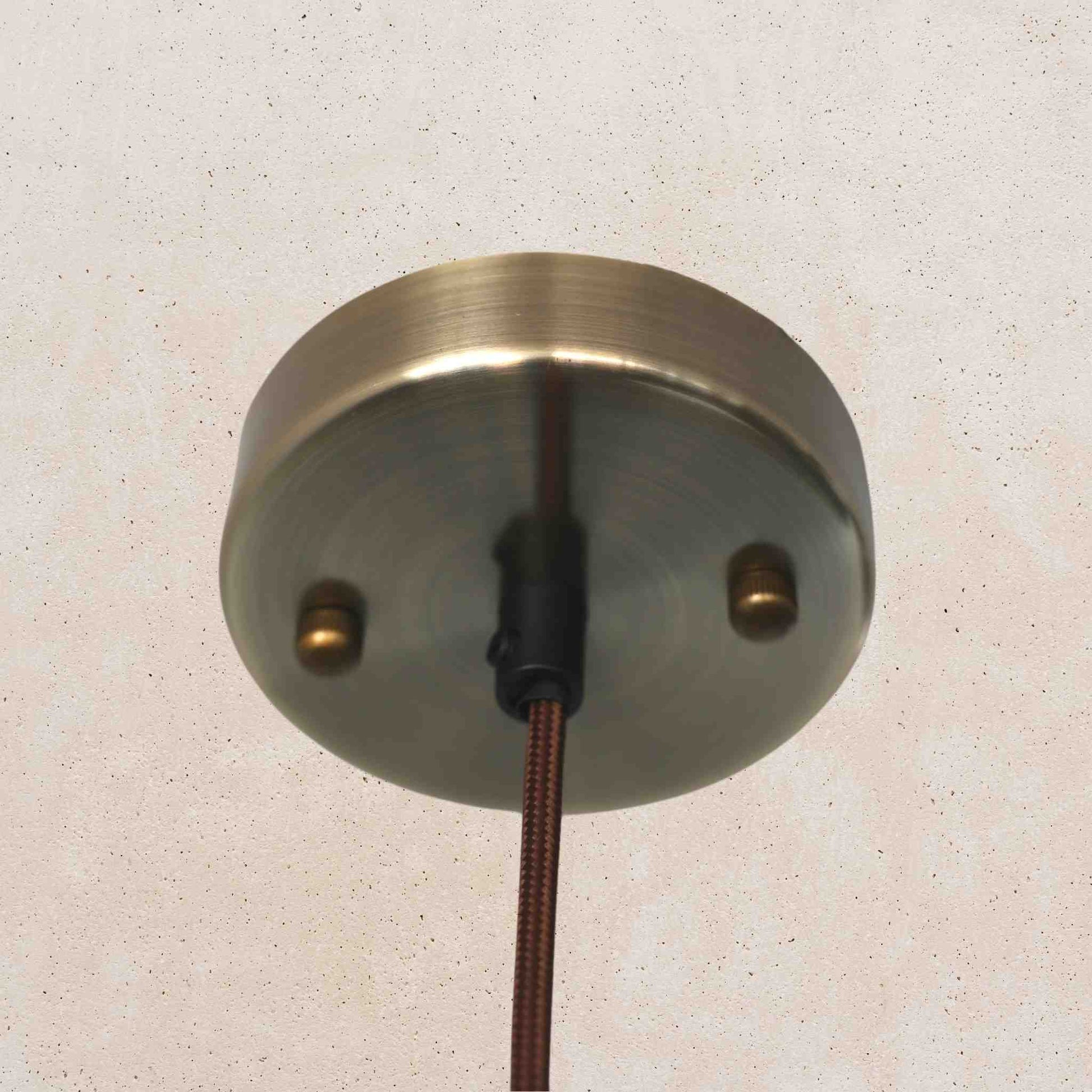 Metallic ceiling rose with wiring on a textured beige wall